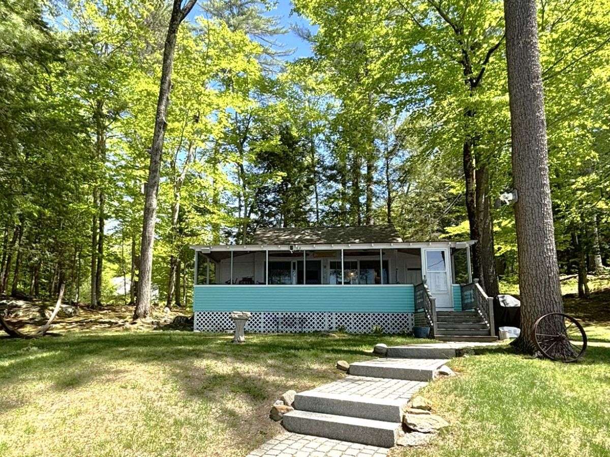 A charming turquoise cottage nestled in a lush, tranquil forest, offering a peaceful woodland retreat just steps away from Webster Lake.