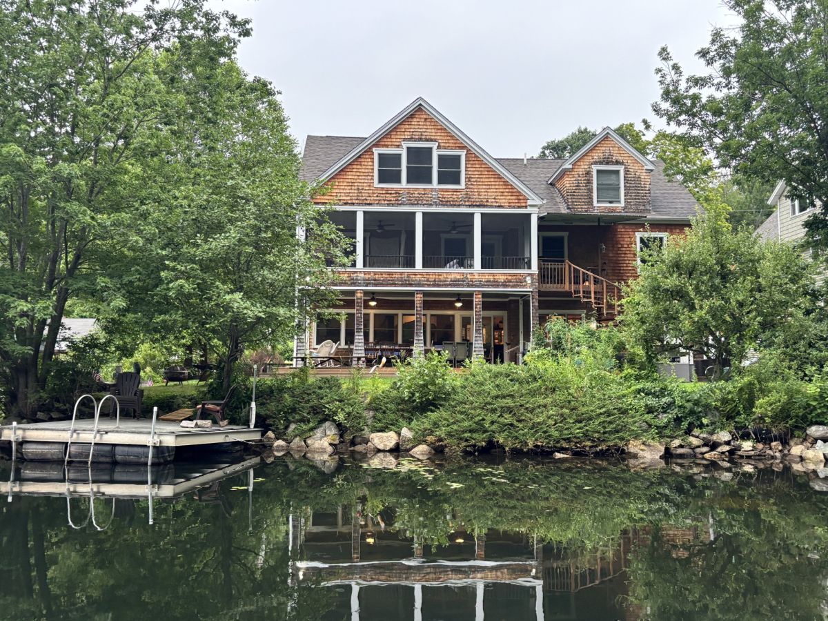 A charming waterfront retreat with natural cedar shingle siding, featuring multiple decks and a private dock for lake adventures. Nestled among lush greenery in a peaceful lakeside setting.